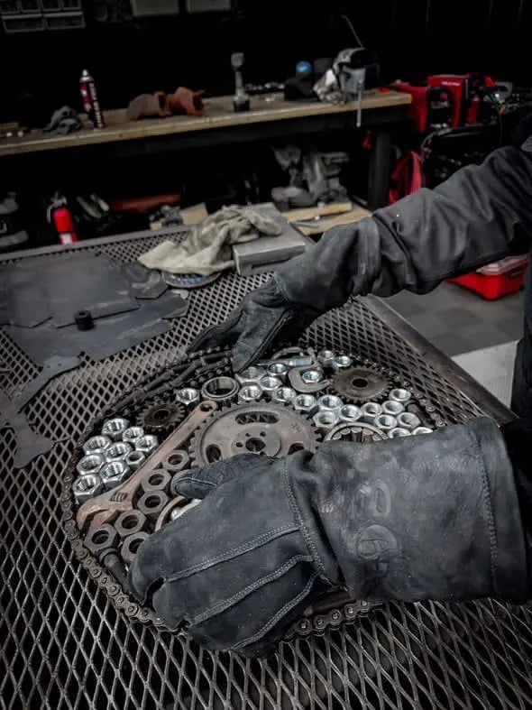Heavy Duty Leather Welding Gloves - Black, rated 4.70, used while assembling metal gears and bolts on a workshop table.