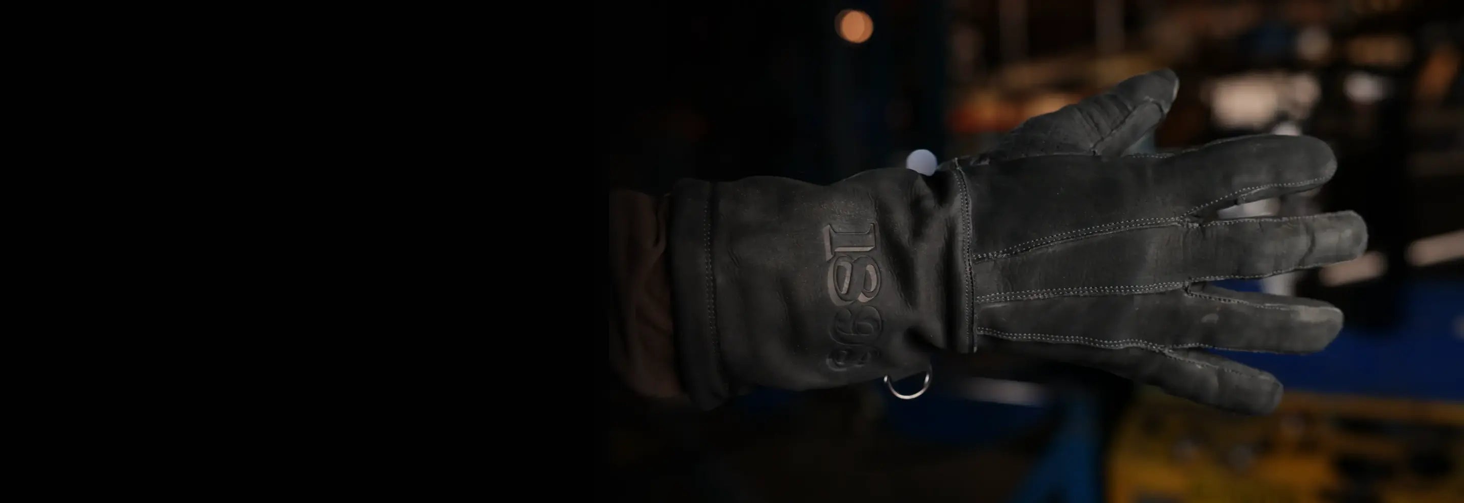 Close-up of leather glove with visible stitching and “1898” embossed on the wrist, worn in an industrial setting, highlighting craftsmanship, heritage, and rugged design – Rated 4.70