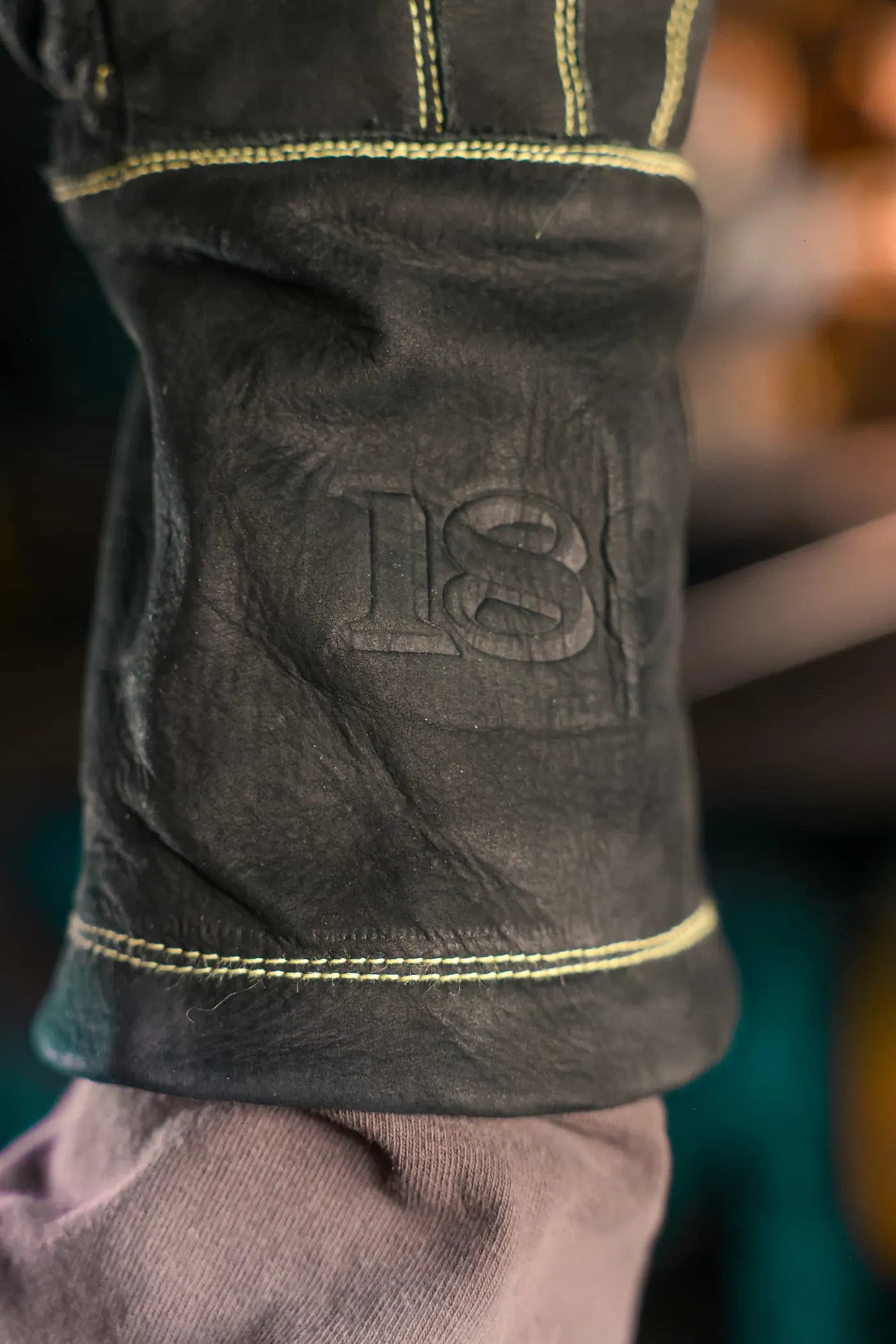 Close-up of leather sleeve with golden thread stitching and embossed “1898” branding, showcasing craftsmanship and premium construction – Gold