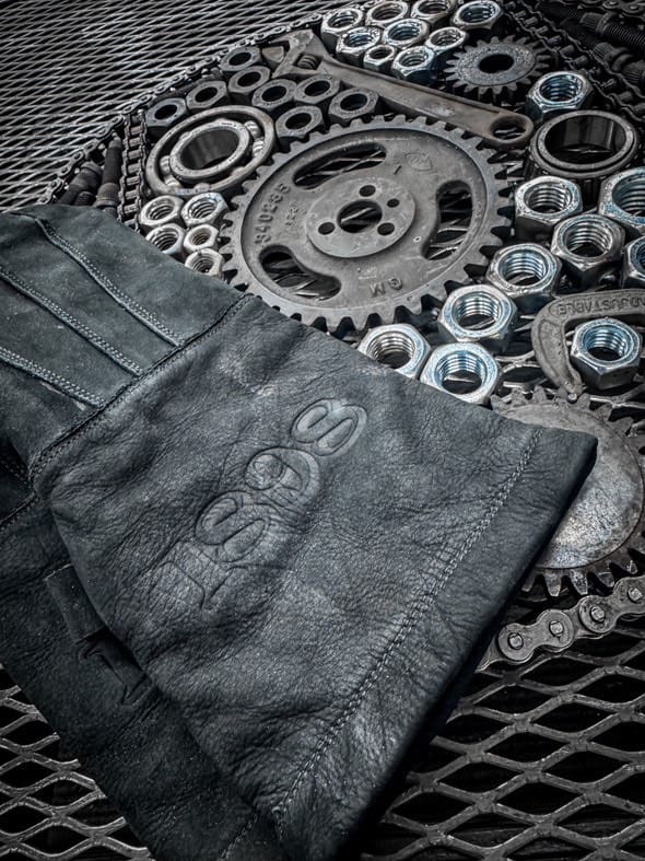 Pair of black leather work gloves with black stitching placed on a metal surface surrounded by gears, bolts, and washers — highlighting craftsmanship, industrial styling, and rugged durability – Rated 4.70 – Black