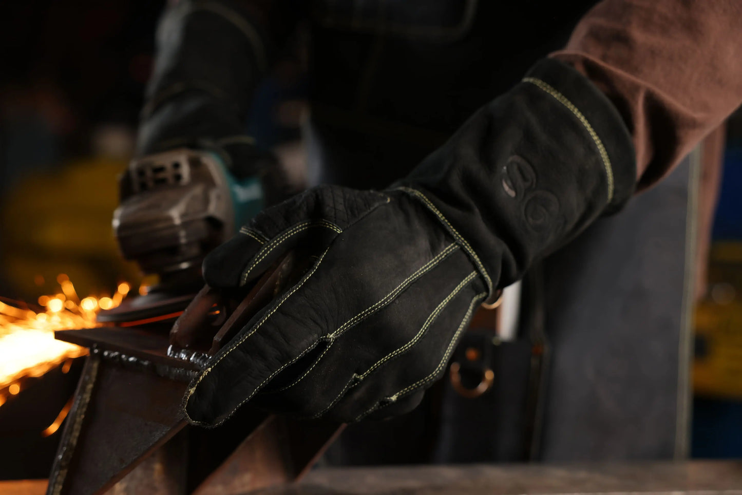 Close up of gold thread leather work gloves worn by a metalworker using a power grinder, with sparks flying showcasing real world protection, grip, and durability in industrial settings Rated 4.60 – Gold