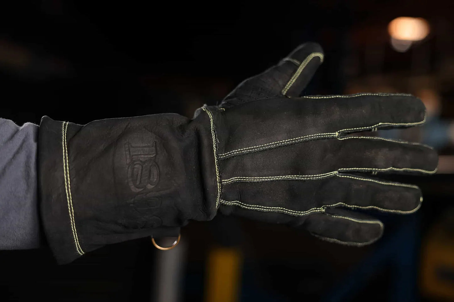 Close up of leather work glove with gold stitching and embossed 1898 logo on the wrist, worn in an indoor setting, highlighting craftsmanship, branding, and premium construction Rated 4.70 – Gold