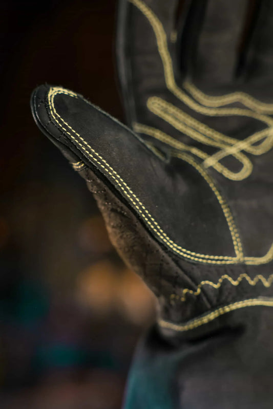 Close-up of leather work glove with gold stitching on the palm and thumb, showing reinforced seams and textured surface for grip and durability – Rated 4.70 – Gold