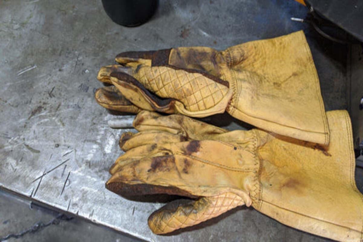 Well-worn pair of tan leather welding gloves from early 1898 Leather testing on a steel workbench