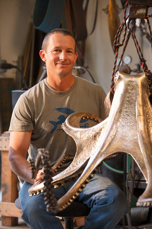 Sculptor Casey Parlette seated beside his large bronze octopus sculpture in the studio