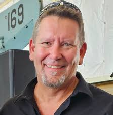 Portrait of metal sculptor Kevin Stone smiling in front of heavy equipment