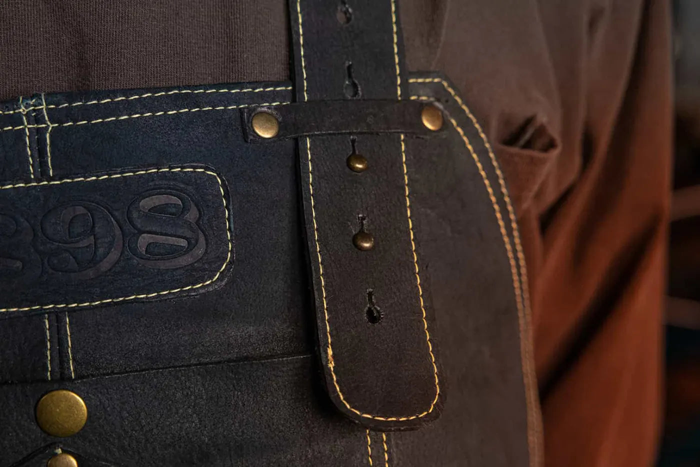 Close-up front view of 1898 Leather welding apron showing gold thread on neck strap and partial 1898 logo high-quality apron rated 4.85 stars for durability and style - Gold