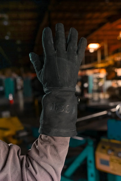 Black thread leather work glove held up in an industrial setting, featuring embossed 1898 brand logo on the wrist and textured leather surface  Rated 4.70 – Black