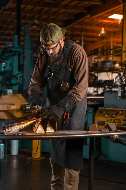 Worker welding metal while wearing 1898 heavy duty leather apron and gloves with black thread stitching and reinforced protection – Black