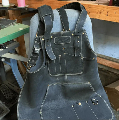 Leather work apron with gold thread stitching, multiple pockets, and metal hardware, draped over a chair — showcasing craftsmanship, reinforced construction, and premium design for tradespeople – Rated 4.85 – Gold