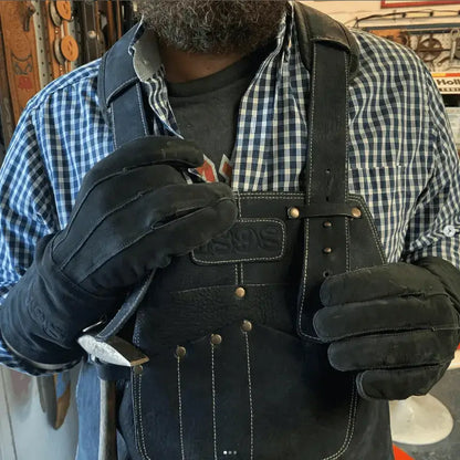 Craftsman wearing a leather work apron with gold thread stitching, metal rivets, and embossed pocket branding, holding a tool in a workshop setting — showcasing durability, craftsmanship, and real-world utility – Rated 4.85 – Gold